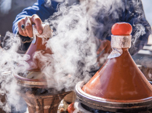 Hand lifting lid off tagine pot and releasing cooking smoke