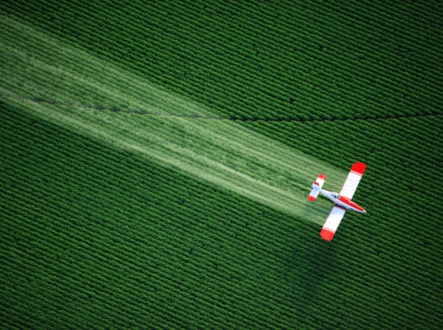 aerial-view-of-a-crop-duster-or-aerial-applicator-flying-low-and-spraying-agricultural-chemicals-over-lush-green-potato-fields-in-idaho